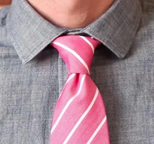 A close-up of a man adjusting his pink tie, demonstrating the technique of tying a tie.