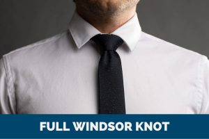 A man showcases the full Windsor knot while wearing a white shirt and black tie.