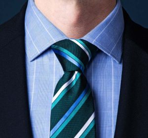 Close-up of a man wearing a blue shirt and green tie, showcasing a method for tying a tie.