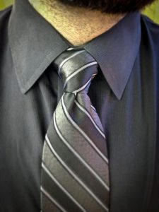 A man dressed in a black shirt and striped tie showcases the process of tying a tie.