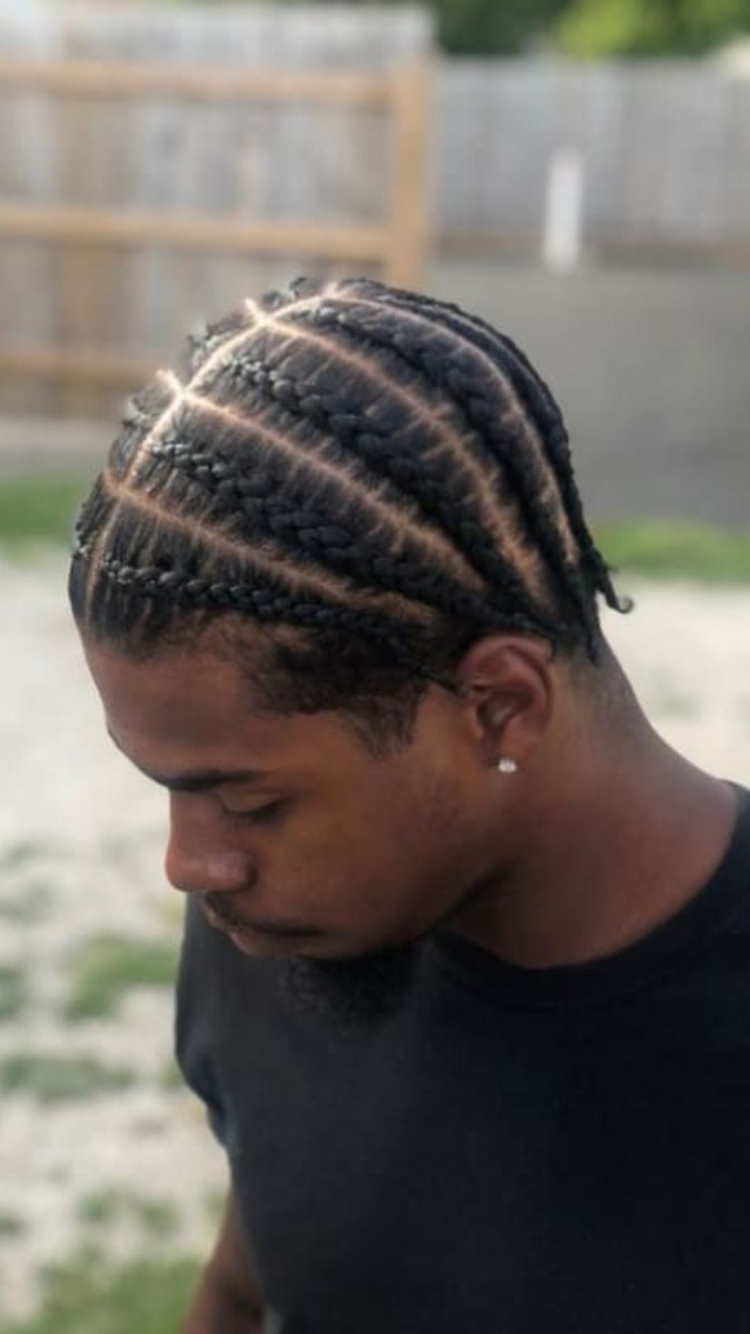  A man wearing a black shirt, showcasing his stylish braided hairstyle.