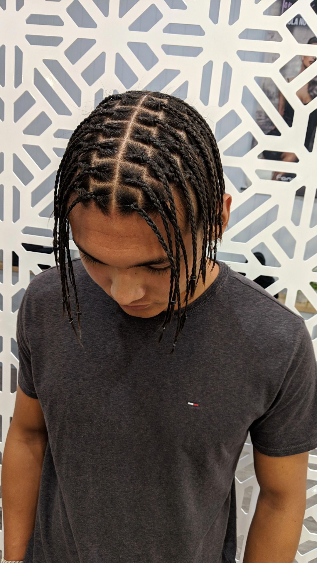 A man with dreadlocks stands against a wall, emphasizing his stylish braid hairstyle and individuality.