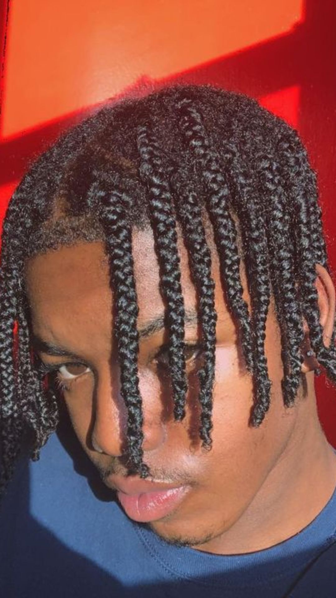 A man sporting dreadlocks and a blue shirt, featuring an eye-catching braid hairstyle.