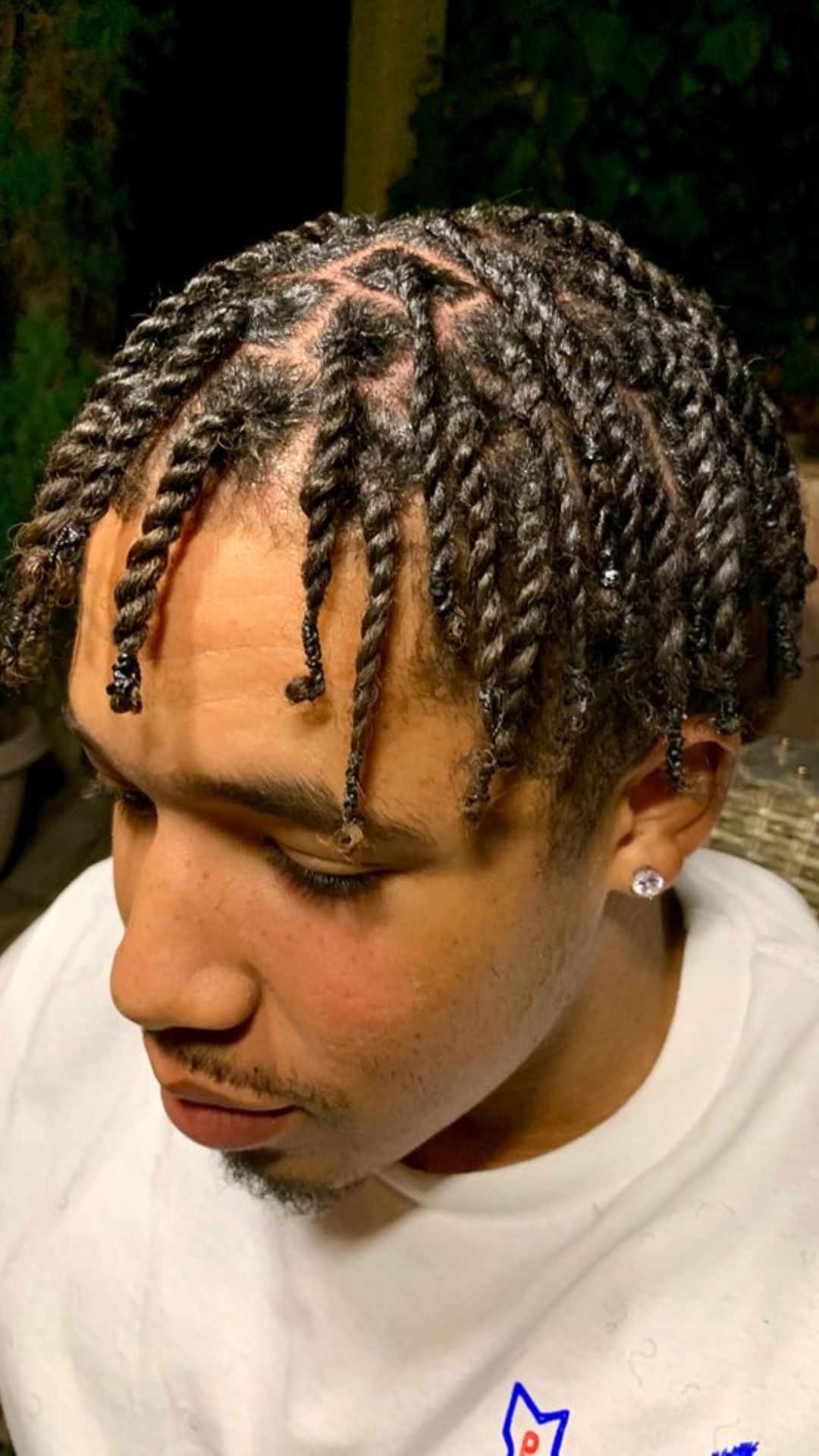 A man with dreadlocks sits comfortably on a bench, displaying his intricate braid hairstyle amidst a serene backdrop.