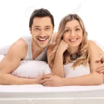 70141952-happy-couple-lying-in-bed-and-looking-at-the-camera-isolated-on-white-background